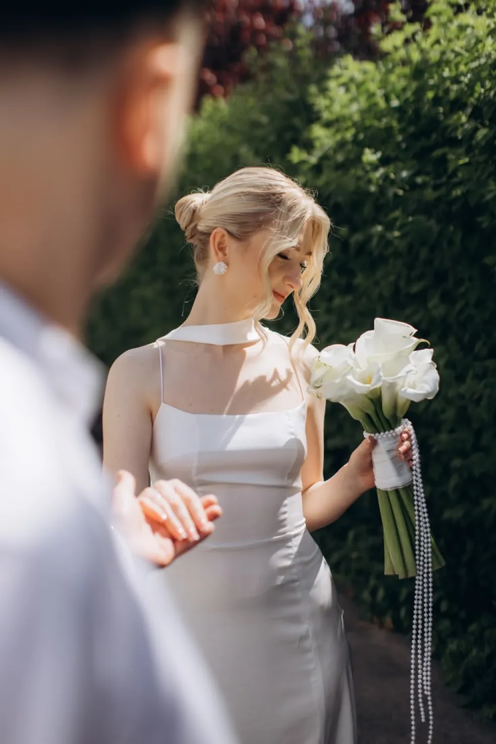Elegantný svadobný účes 2026 s nízkym blond drdolom, voľnými zvlnenými pramienkami okolo tváre a nevestou v saténových šatách