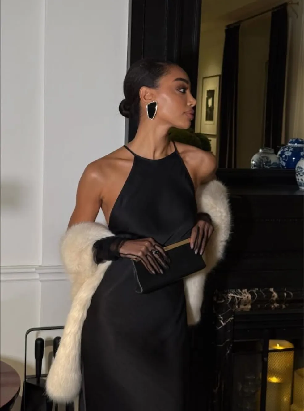 Elegantný outfit na zimnú svadbu: žena v dlhých čiernych spoločenských šatách s odhalenými ramenami, bielou kožušinovou štólou a čiernou kabelkou