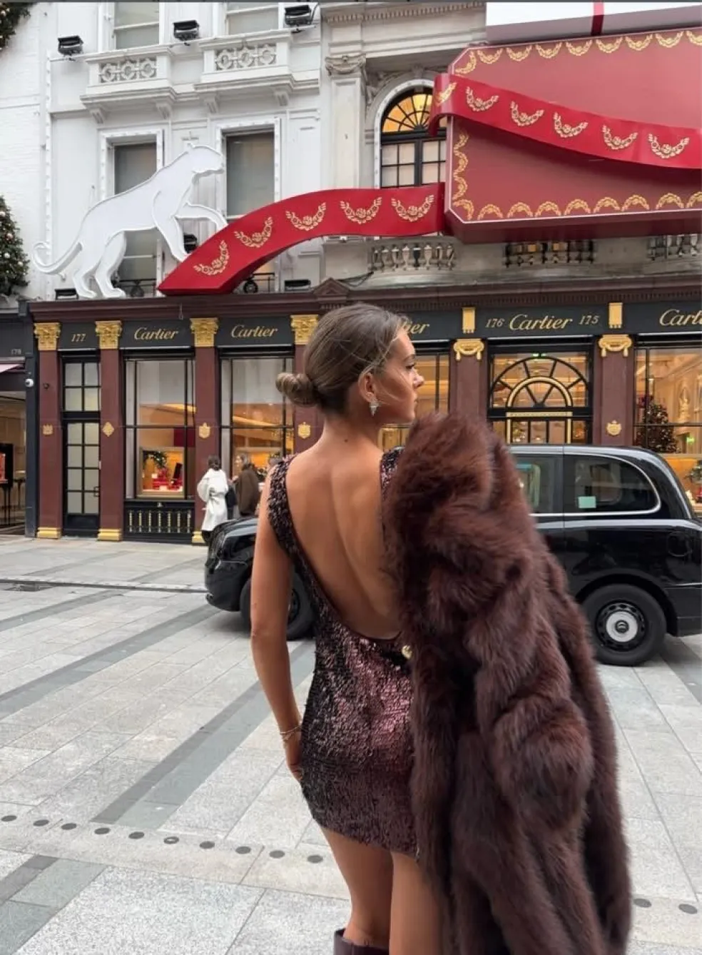 Elegantný outfit na zimnú svadbu – krátke trblietavé spoločenské šaty s odhaleným chrbtom doplnené hnedým kožušinovým kabátom